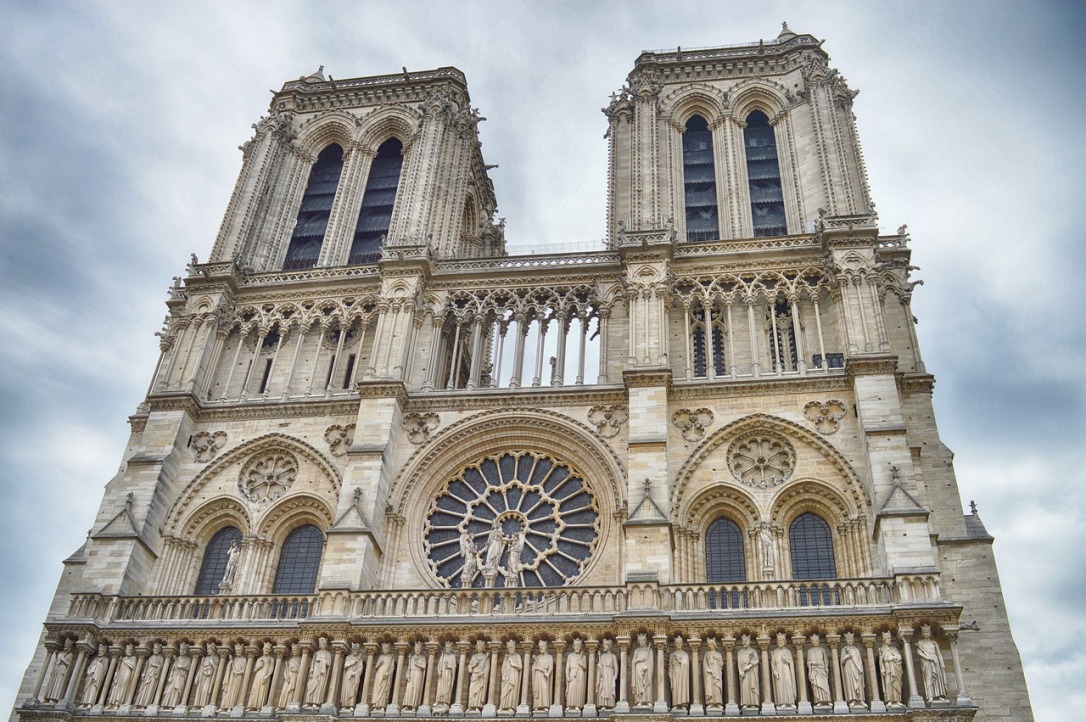 IMage shows the outside of Notre Dame Cathedral. It is a large gothic structure with many statues and flying buttresses.
