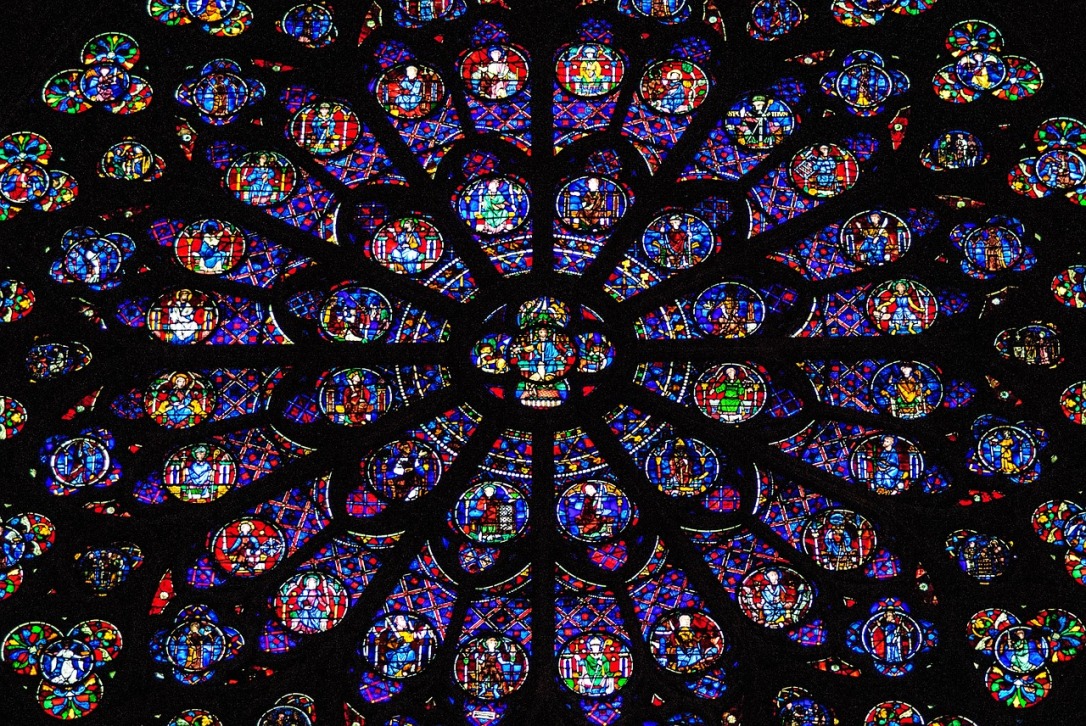 An image shows the stained glass of the rose window in Notre Dame. The window is circular with many bright colors. The window panes look like flower petals