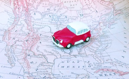 A small red toy car sits on a road trip